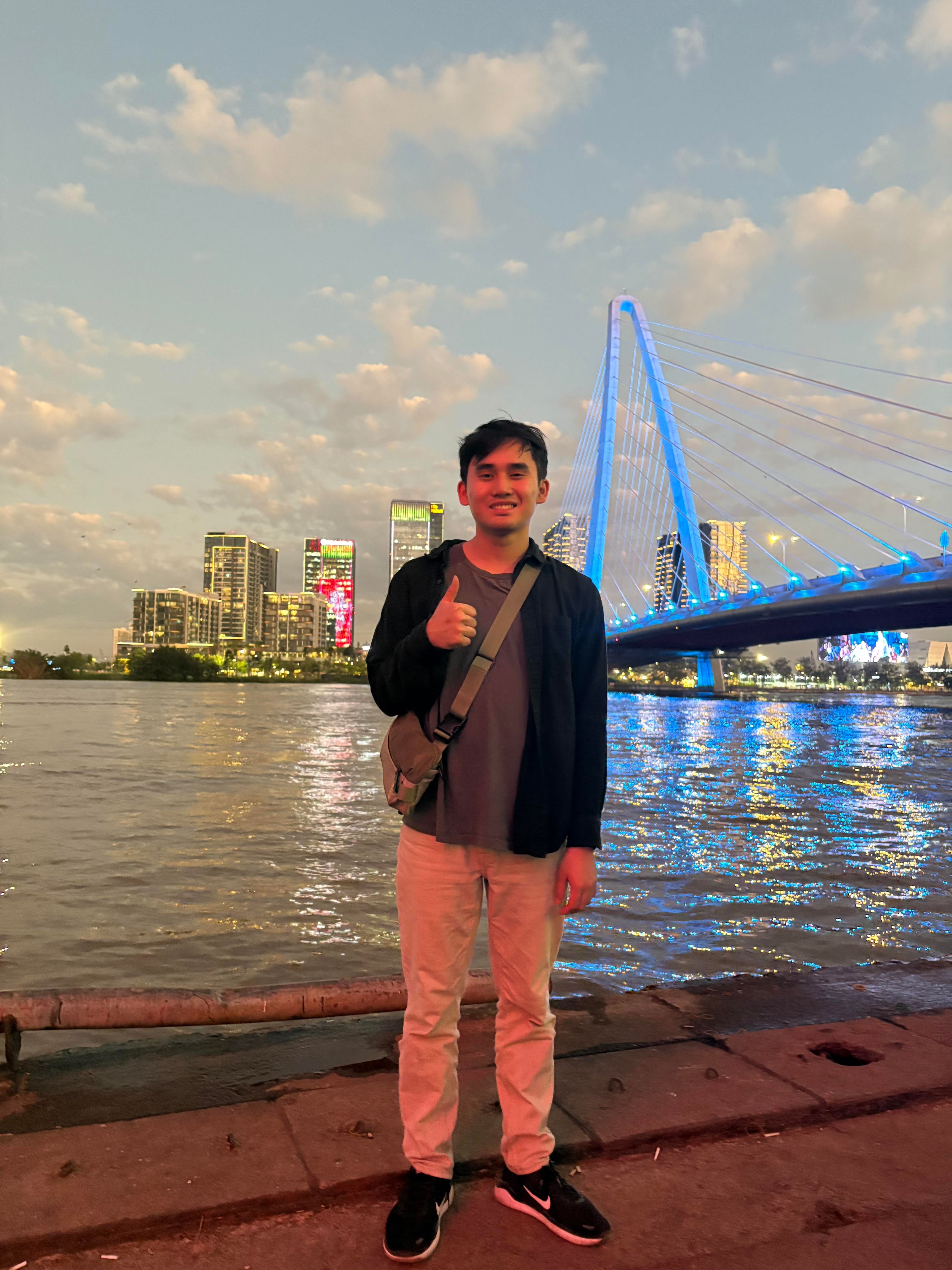 Brian Pham standing by the waterfront at sunset with a bridge in the background.